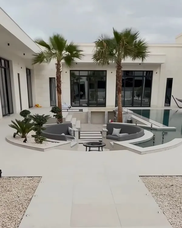 A complete view of a luxury villa's outdoor space, featuring a sunken seating area, a pristine pool, and carefully placed palm and bonsai trees to create a modern oasis.