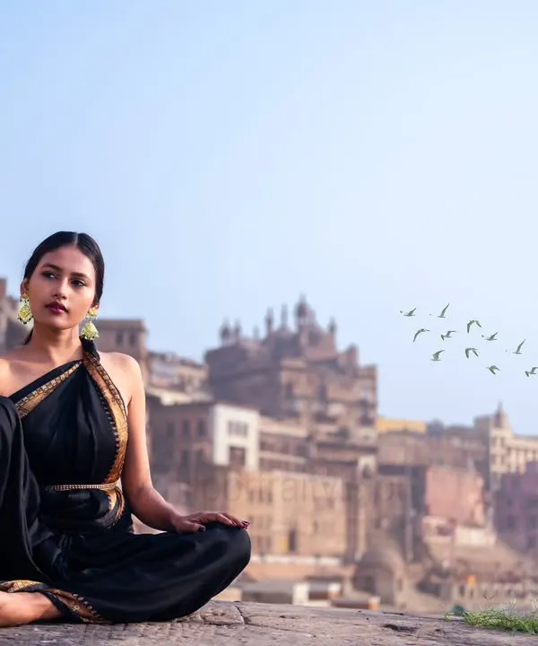 A moment of peace against the timeless backdrop of the Banaras ghats. The elegance of the black saree contrasts with the ancient city, creating a portrait of serene contemplation.