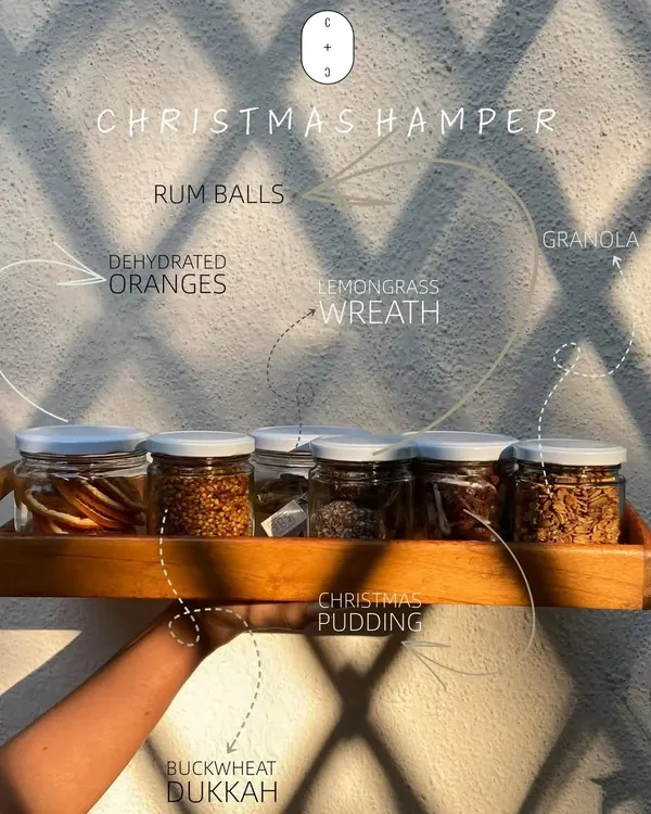 A look inside our Christmas hamper. It features a variety of our handmade goodies like rum balls, granola, Christmas pudding, and even a lemongrass wreath, all beautifully arranged.