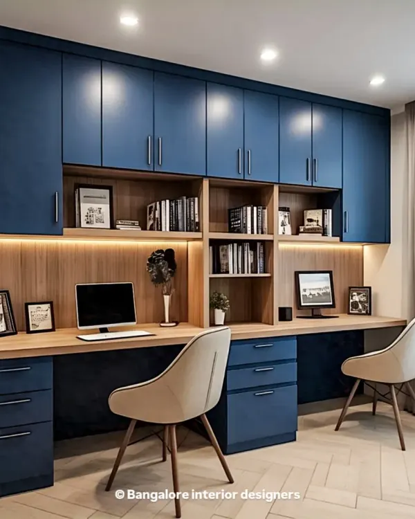 A sophisticated home office for two, featuring deep blue cabinetry that provides extensive overhead storage. The long wooden desk offers ample workspace, and under-cabinet lighting ensures the area is well-lit.