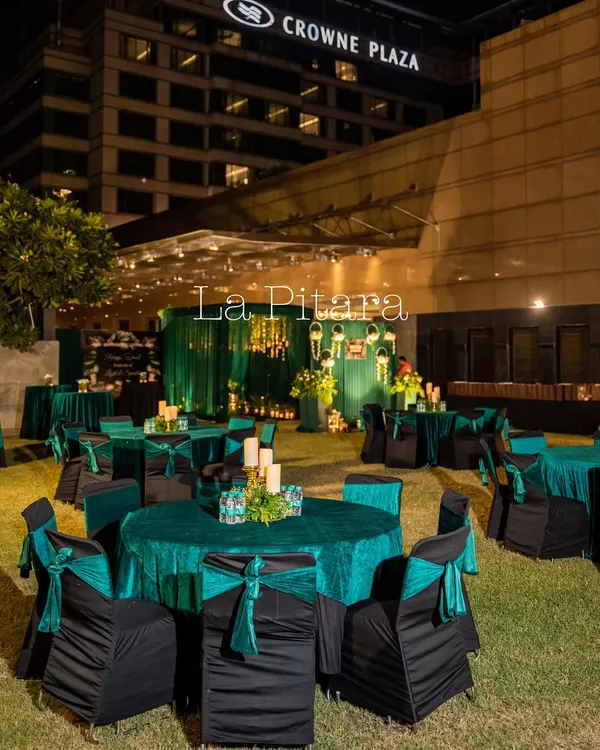 An outdoor setup for the Inditex Diwali party at Crowne Plaza. The guest seating featured round tables with elegant emerald green cloths and black chair covers with matching sashes, creating a chic and uniform look.