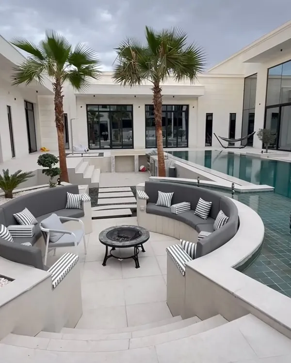 For this luxury villa, we designed a stunning poolside landscape with a sunken seating area, fire pit, and strategically placed palm trees. The clean white stone and calm water are perfectly balanced by the greenery, creating a resort-like feel right at home.