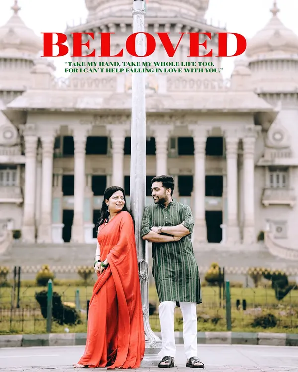 A grand, symmetrical shot of a couple in traditional wear standing before the Vidhana Soudha in Bangalore, framed as a 'Beloved' movie poster.