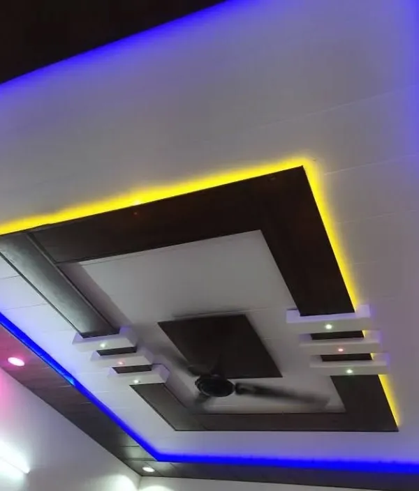 A modern PVC ceiling design with a dark wood-finish frame. The dual-color lighting, with yellow on the inside and blue on the outside, creates a striking contrast.