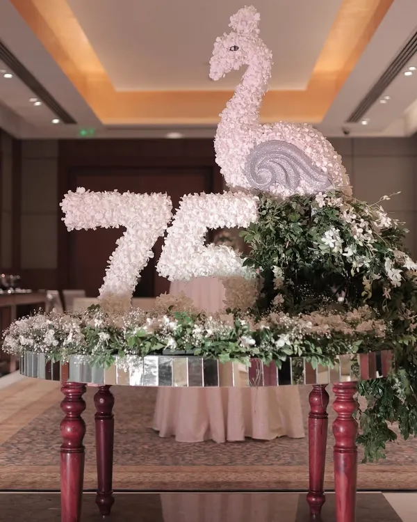 A full view of the custom floral sculpture we created for a 75th birthday. The piece, featuring a swan and the number "75" made entirely of white flowers, sits atop a mirrored table, serving as a magnificent focal point.
