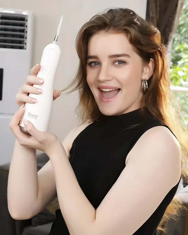 An international model holds up a white water flosser with an excited expression, creating a positive and engaging lifestyle shot for a personal care brand.