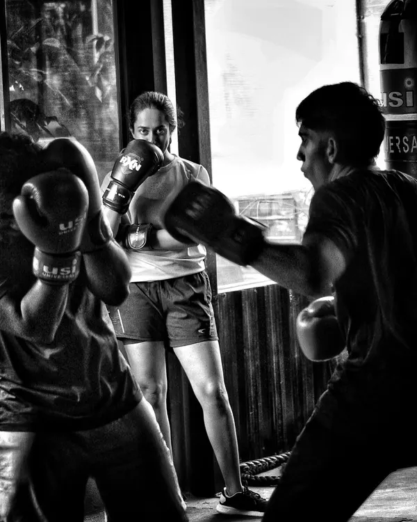 A female boxer watches a sparring session, studying technique. Learning happens both inside and outside the ropes.
