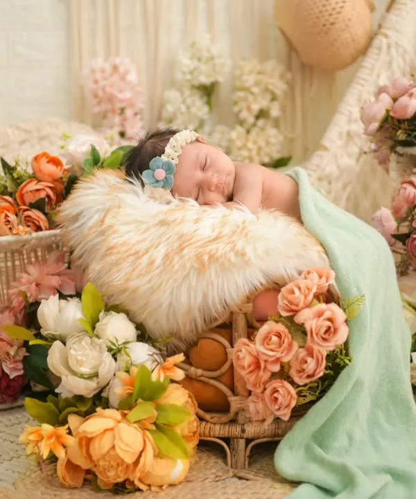 A newborn sleeps peacefully amidst a lavish arrangement of peach and white flowers. This floral-themed setup is one of our specialties, creating a dreamy, garden-like atmosphere for a truly enchanting portrait.