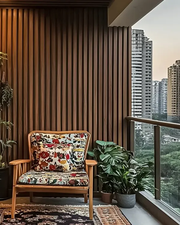 A cozy balcony corner with a comfortable armchair and lush green plants. The vertical wood fluting on the wall adds warmth and texture, creating a perfect reading nook with a city view.
