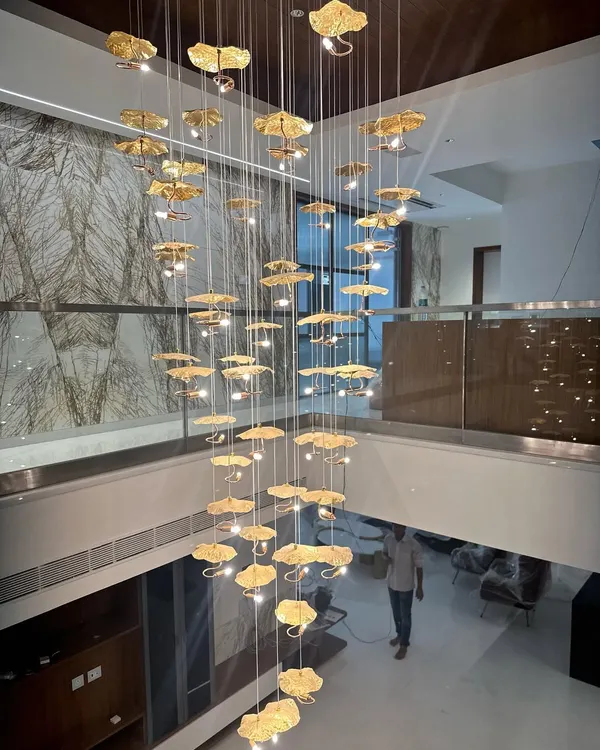 This magnificent cascading chandelier is the centerpiece of a double-height foyer. Each leaf-like element is crafted from gold-toned metal, creating a stunning sculptural light fixture that is both art and illumination.
