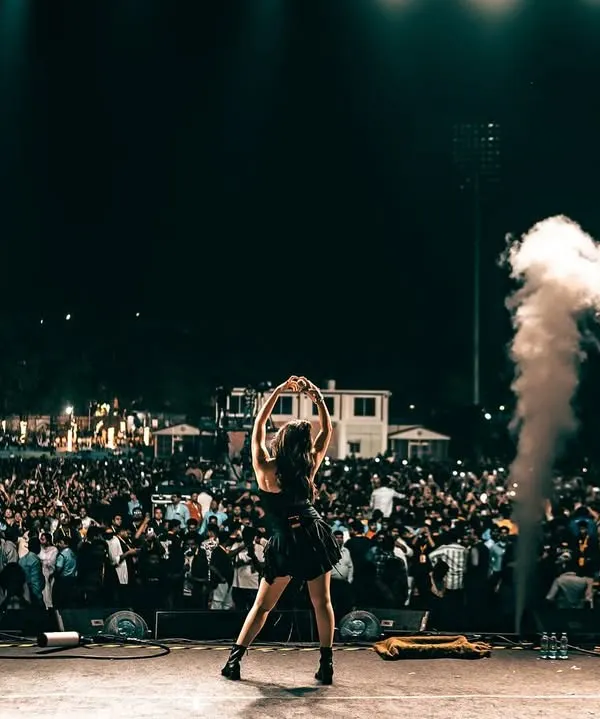 The energy of a live show. Dhvani Bhanushali commands the stage in a custom black fringed top from Seraphine Design Studio, surrounded by smoke and spotlights.