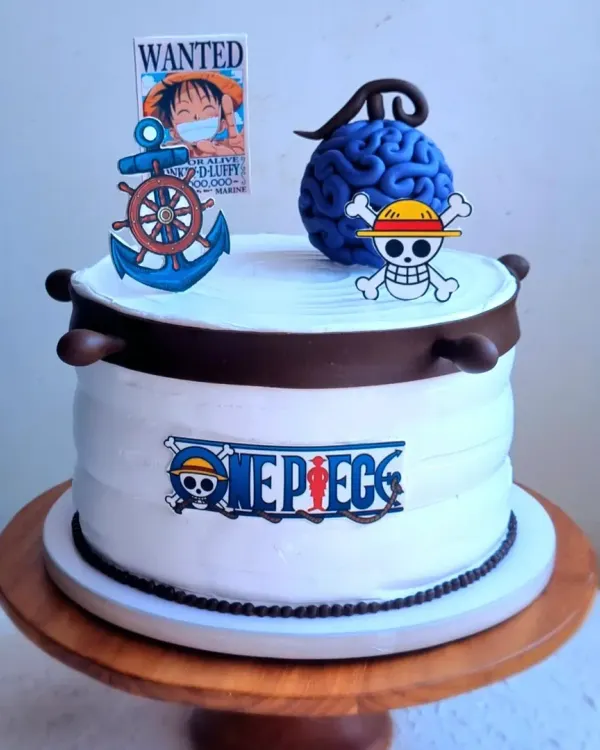 A whipping cream cake with a "One Piece" anime theme. The cake is decorated with printed toppers of the logo, a wanted poster, and a sculpted Devil Fruit.