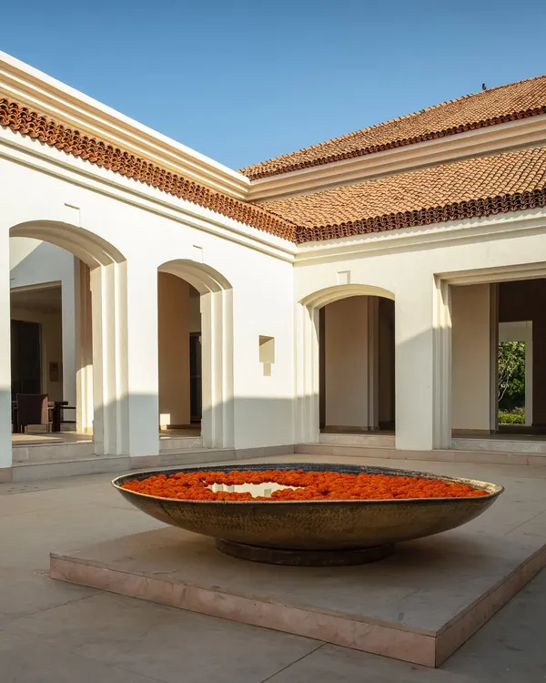 An 'urli' filled with marigolds sits at the heart of a sunlit courtyard, a traditional welcome that grounds the space in Indian heritage and offers a moment of peace.