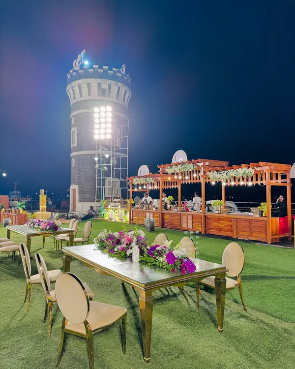 A stunning outdoor event space with our rustic wooden food counters set against the backdrop of a historic tower. The elegant guest seating in the foreground shows how we integrate our catering setup into the overall event design.