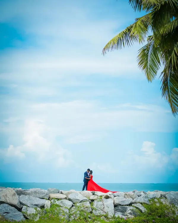 A breathtaking pre-wedding shot of a couple by the sea, with a vibrant red dress creating a stunning contrast against the blue sky. We specialize in creating epic, wide-angle shots at beautiful beach locations.