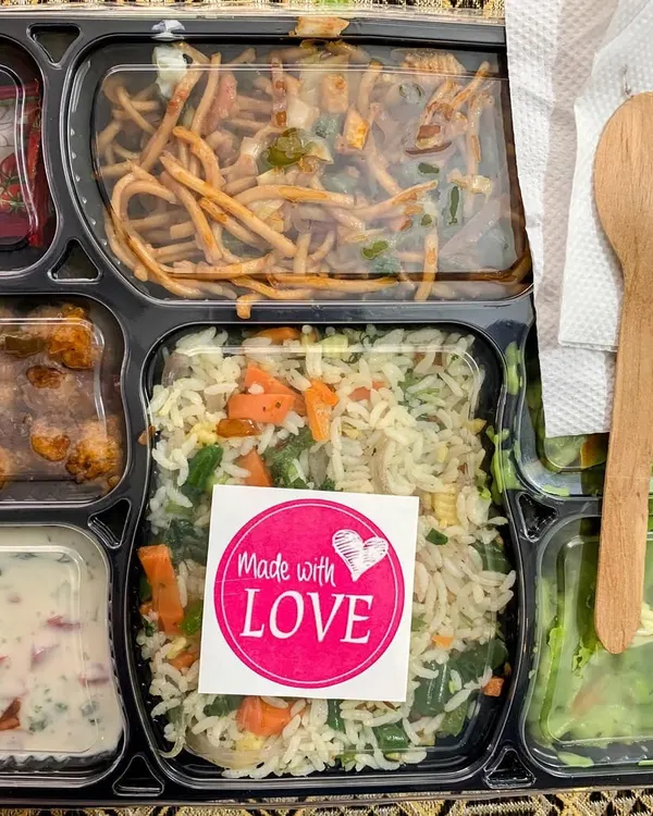 A complete meal in a box, sealed with love. This thali features my signature Veggie Pulao, Babycorn Manchurian, Hakka Noodles, Green Sauce Pasta, and a fresh salad, complete with a wooden spoon for easy eating.