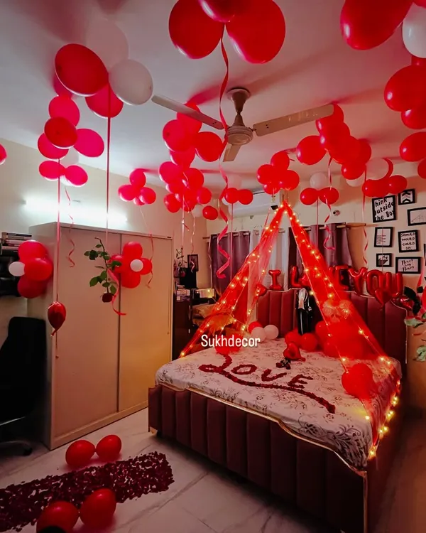 This is my signature romantic room decoration. I transform the entire space with hundreds of red and white balloons covering the ceiling, a beautiful canopy over the bed lit with warm fairy lights, and the word 'LOVE' written in rose petals for a truly immersive and magical surprise.