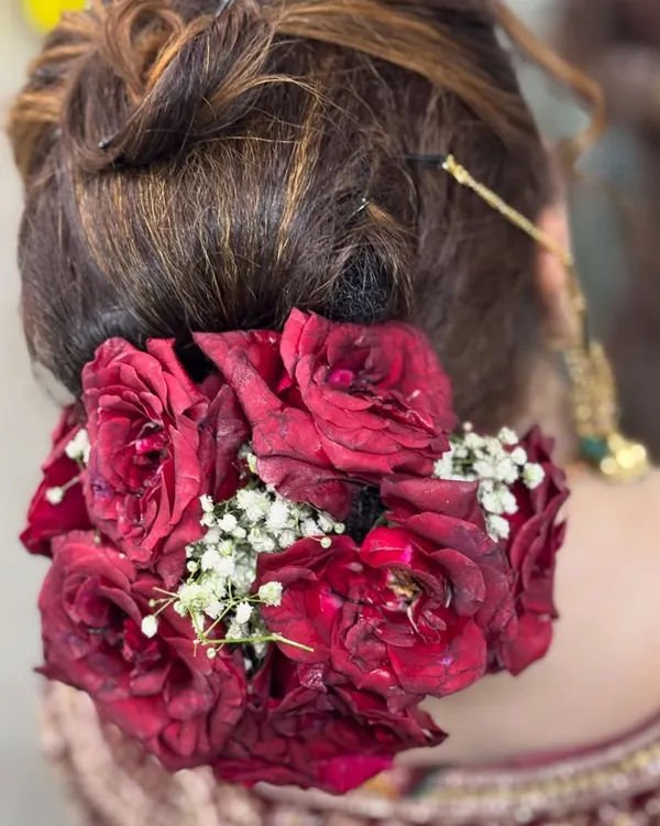 A close-up of a beautiful and traditional bridal bun, adorned with fresh red roses and delicate baby's breath flowers.