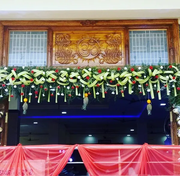 A beautifully crafted traditional garland to adorn the entrance of a home or venue. This design uses woven coconut leaves, red roses, and baby's breath for a welcoming and auspicious look.