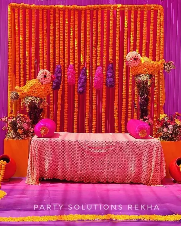 A perfect stage for a Haldi ceremony, glowing with tradition. I used a backdrop of dense marigold strings, accented with purple and pink, and quirky bird motifs made of flowers to create a truly unique and colorful setting.