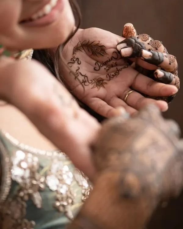 The process begins. Our artist carefully applies the couple's names, 'Jaimin & Krishna', on the bride's palm. This is the start of a beautiful, personalized design.