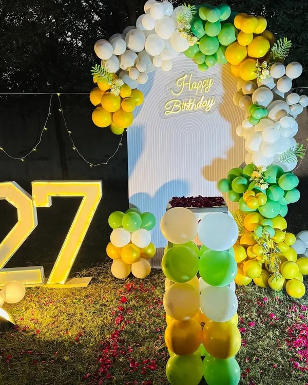 A beautiful outdoor birthday setup for a 27th birthday. This decoration features a balloon arch, a "Happy Birthday" neon sign, and large light-up numbers with the name "Amar".