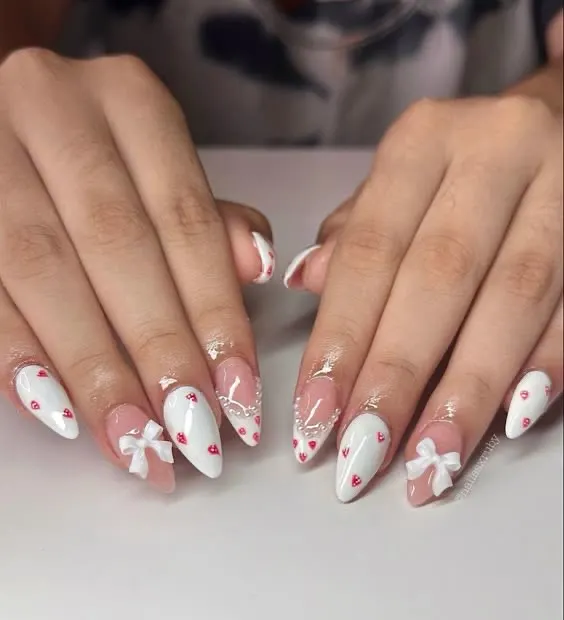 The cutest coquette-style nails. This set features white tips, tiny red hearts, and adorable 3D white bows.
