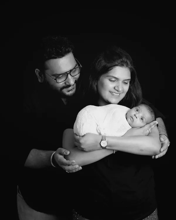 A classic family portrait in black and white. The dark background makes the family the sole focus, highlighting their loving embrace and connection.
