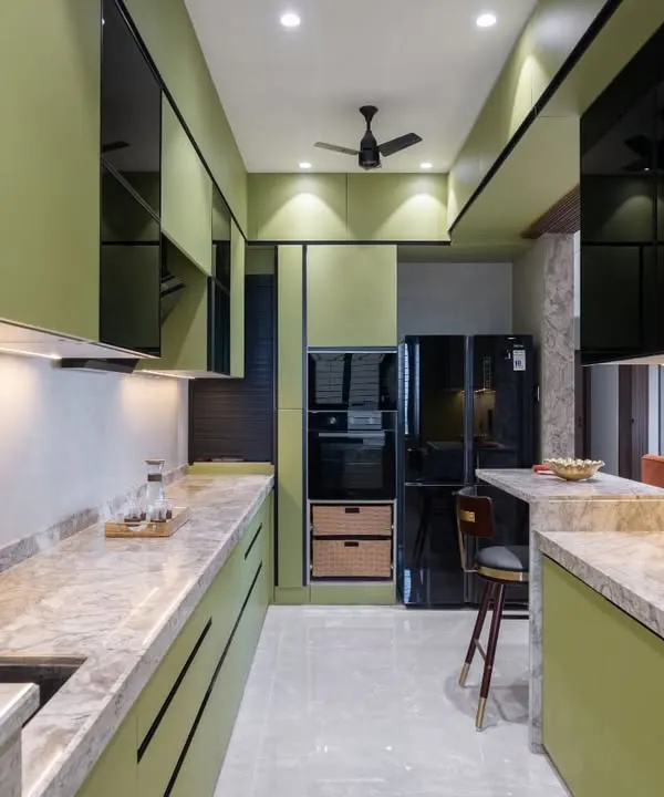 A full view of a modern sage green kitchen, designed to be both a functional workspace and the heart of the home. The handleless cabinets, marble-patterned countertop, and integrated breakfast bar create a clean, contemporary look perfect for family gatherings in this Kalyan residence.