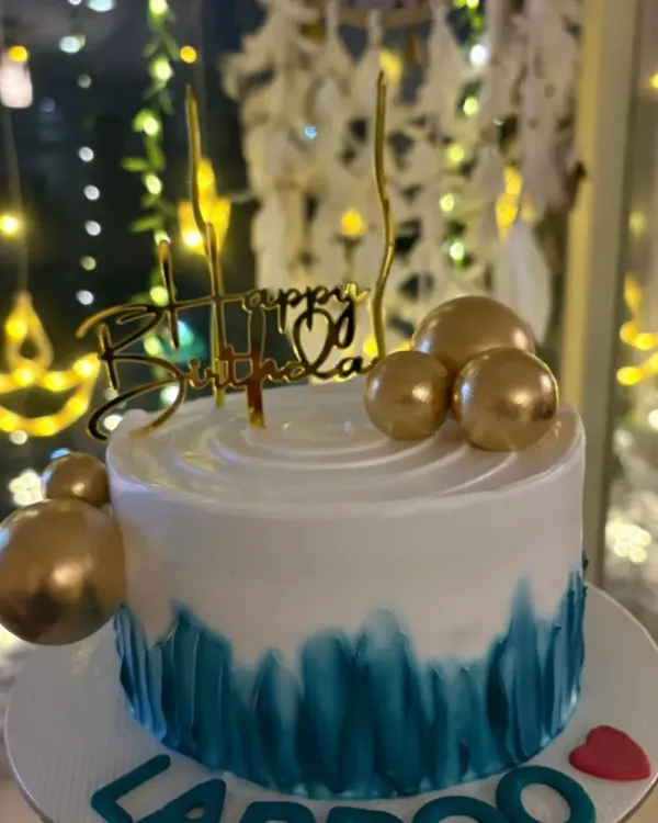A stylish birthday cake with a teal brushstroke effect and gold sphere decorations.