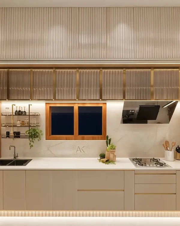 This view of the kitchen highlights the functional layout, with the sink and stovetop integrated into a seamless countertop. The fluted glass overhead cabinets, framed in brushed brass, provide elegant storage, while under-cabinet lighting ensures the workspace is both beautiful and practical. The design combines modern aesthetics with warm, tactile materials for a timeless feel.