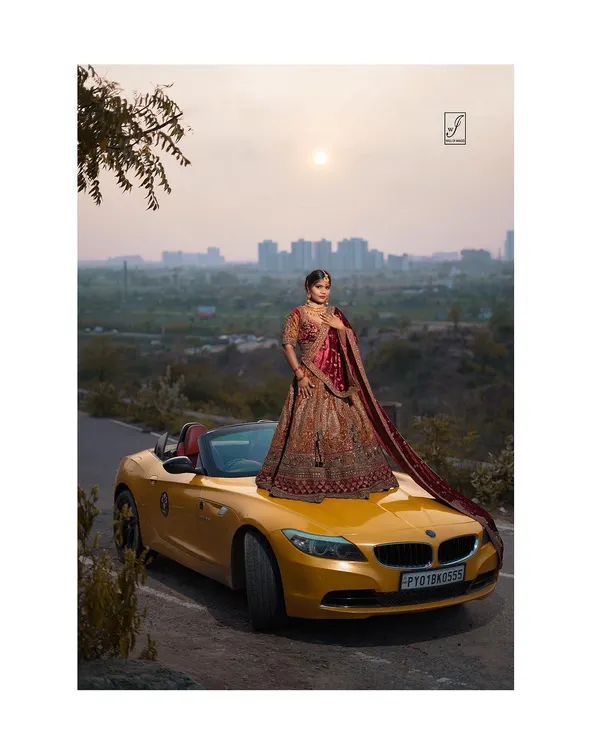 A full-length shot showcasing an intricately embroidered bridal lehenga. Posing the model on a luxury car adds a modern, aspirational twist to traditional bridal photography, creating a truly unique campaign image.
