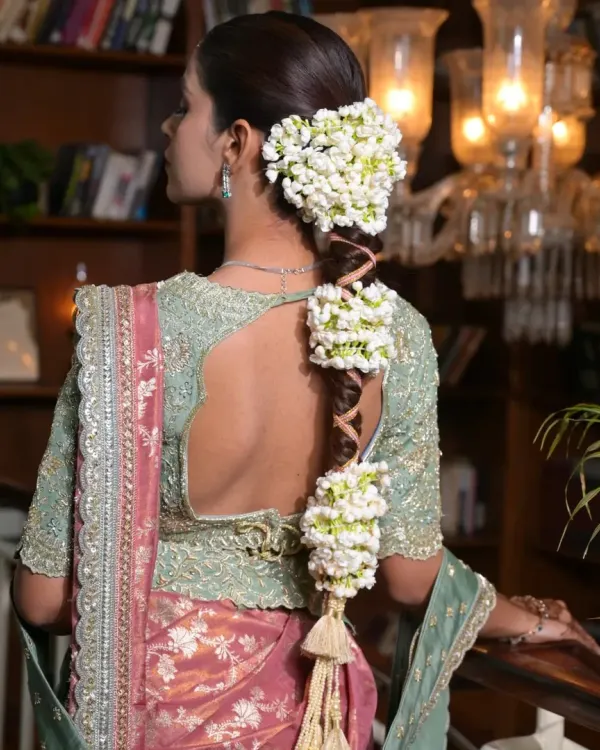 A detailed profile of a traditional South Indian bridal hairstyle. The focus is on the thick, woven gajara braid, heavily adorned with fragrant jasmine flowers for an authentic and rich look.