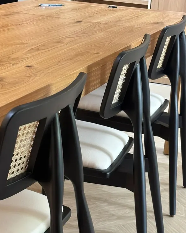 A set of my custom dining chairs with black frames, white cushions, and a cane back detail, paired with a solid oak table. This is a great example of my modern dining furniture.