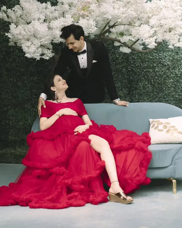 A glamorous maternity look for a studio photoshoot. The mom-to-be looks stunning in a bold red gown, with makeup that highlights her features and gives her a radiant glow.