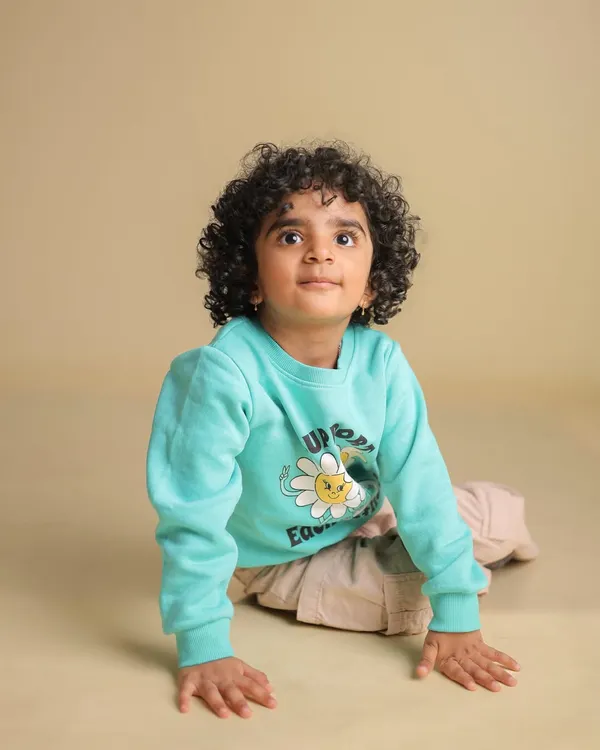 A simple and sweet studio portrait of a toddler with beautiful curly hair, looking up with a curious expression. The neutral background keeps the focus entirely on the child.