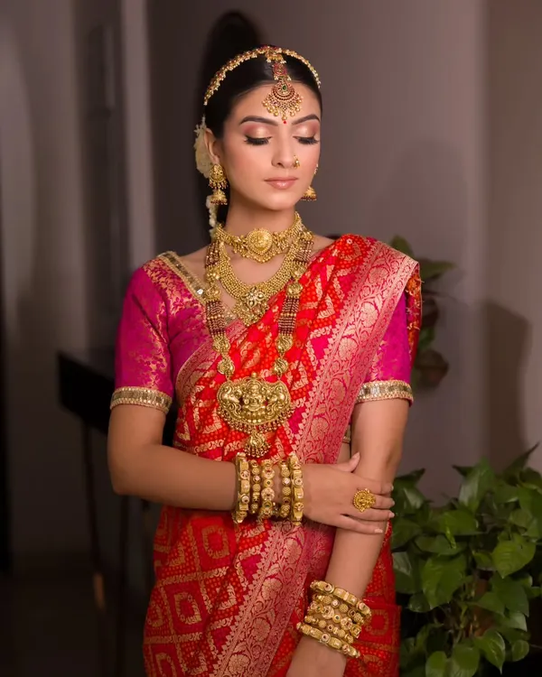 The complete vision of a South Indian bride. Dressed in a traditional red and pink silk saree with magnificent temple jewellery, her makeup is kept classic and golden to enhance her divine look.