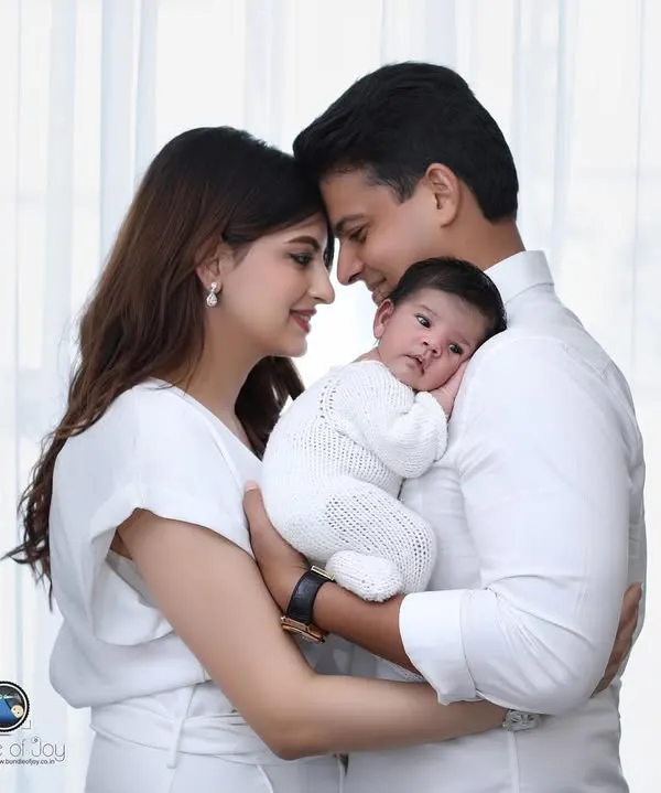 A classic family portrait capturing the tender moment between new parents and their baby. The coordinated white outfits and soft window light create a timeless and pure look.