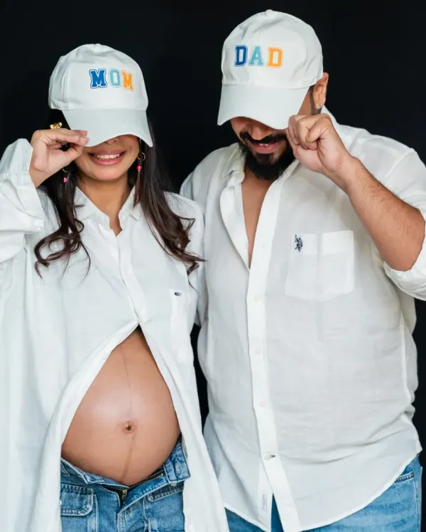 Studio sessions can be fun and modern. Using simple props like 'Mom' and 'Dad' caps, we created a playful and stylish portrait that shows off the baby bump and the couple's personality against a clean, classic black backdrop.