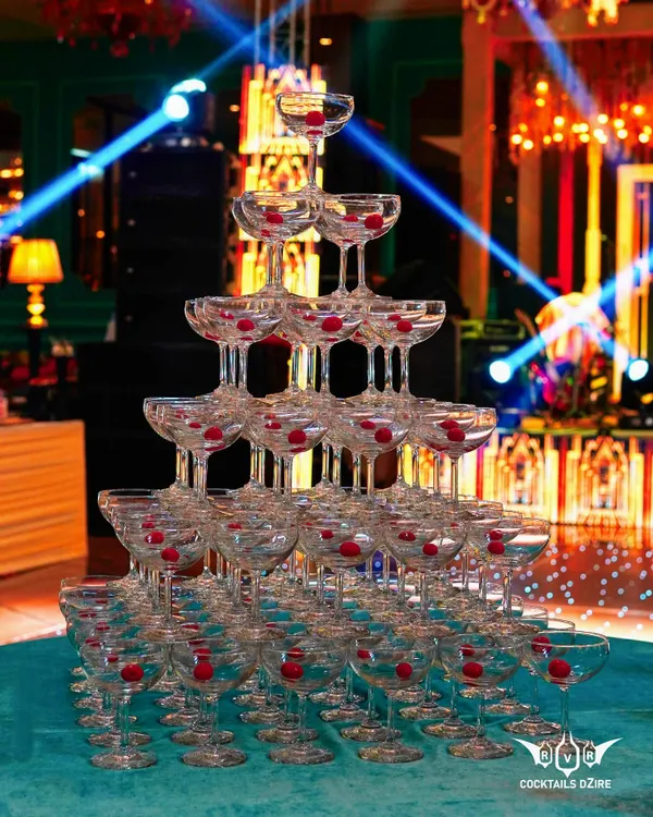 A magnificent champagne tower stands ready for the celebration. Lit by spotlights, the tower is built from dozens of glasses with cherries, waiting for the first pour.