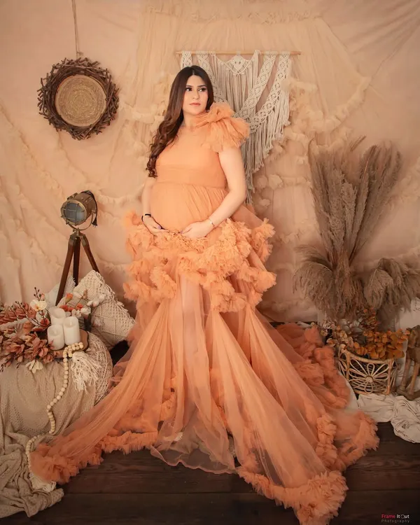 A stunning solo portrait in our boho-chic studio setup. The mom-to-be looks like a goddess in this elaborate peach ruffled gown, surrounded by soft, earthy tones.
