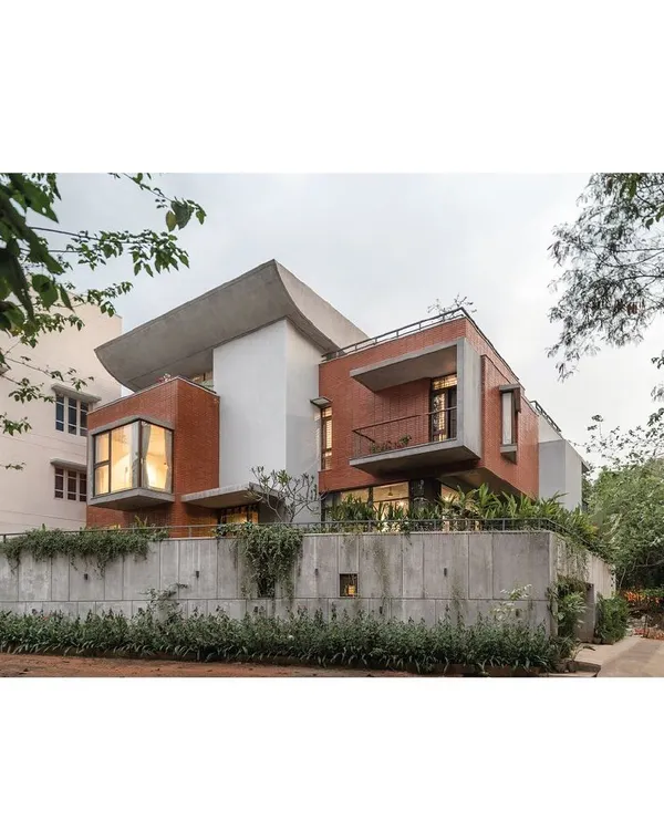 This is the Nairy Residence, a home designed for three generations on a trapezoidal corner site. The structure acts as a protective fortress at street level, while the upper levels open up, becoming porous to the surrounding light and landscape. The curved concrete roof and exposed brick volumes are a direct expression of this dual concept.