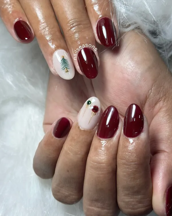 Getting into the festive spirit with this Christmas nail art. A deep, glossy maroon paired with a nude accent nail featuring a hand-painted Christmas tree and holly.