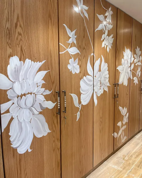 A full view of a series of wardrobe shutters hand-painted with a continuous design of white wildflowers. This project turns a functional storage unit into a seamless, flowing piece of botanical art.