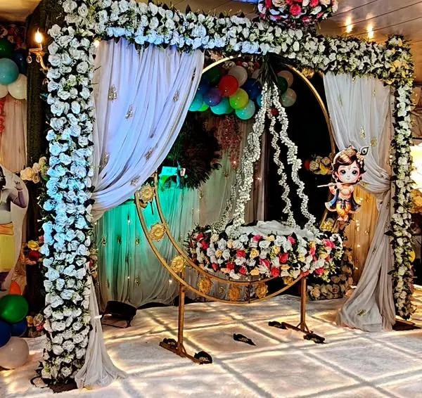 A gorgeous Krishna-themed naming ceremony decoration. The setup includes a decorated cradle under a floral arch, character cutouts, and an LED-lit stage, creating a blessed and beautiful environment for the 'palna' ceremony.