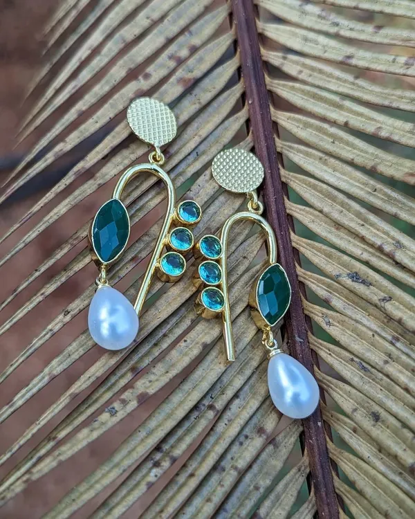 Add a pop of green to your look with these stunning brass earrings. The design features green stones and a delicate pearl drop, making them perfect for both western and Indian wear.