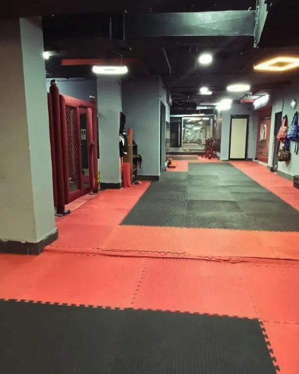 A view of our training floor, with the MMA cage on the left and a clear path for drills and conditioning. The red and black mats mark the zone where you leave your excuses behind.
