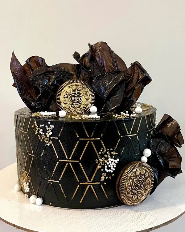 This design is all about texture and contrast. I used a geometric stencil on black buttercream to create a modern pattern, highlighted with gold. The cake is topped with abstract chocolate sails and gold-dusted Oreo cookies for a truly unique look.