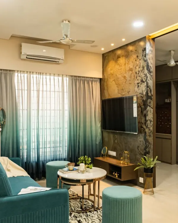 A view of the completed living room, featuring a teal sofa, ombre curtains, and a TV unit set against a dark stone veneer wall. The design balances bold colors with warm, natural textures.