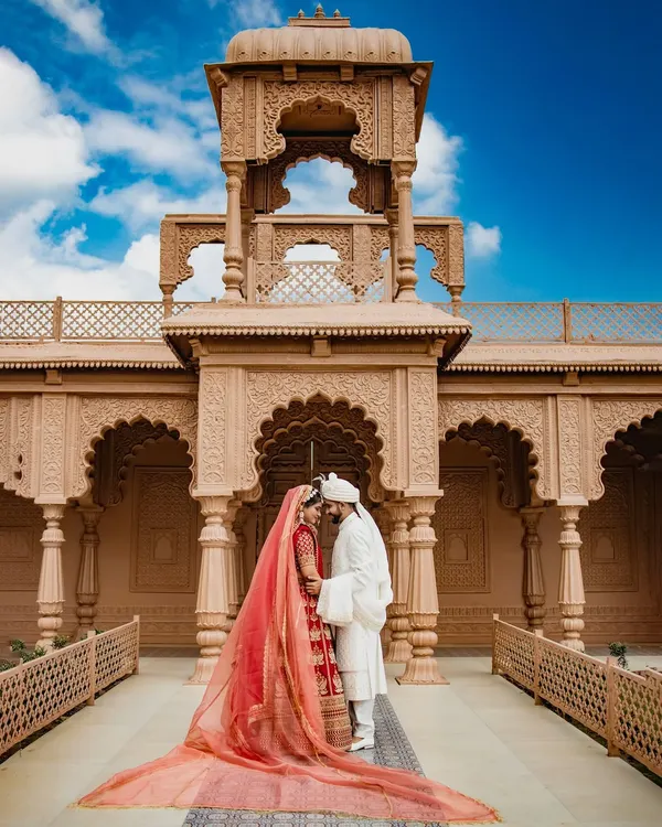 This is the kind of fairytale moment I live to capture. The grandeur of the location is matched only by the love between the couple, with her magnificent red lehenga and trailing veil creating a truly timeless portrait. This is more than a photo; it's the centerpiece of a royal love story.